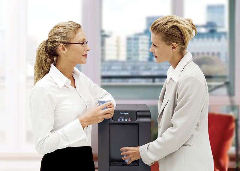 Female Co Workers drinking water by printer