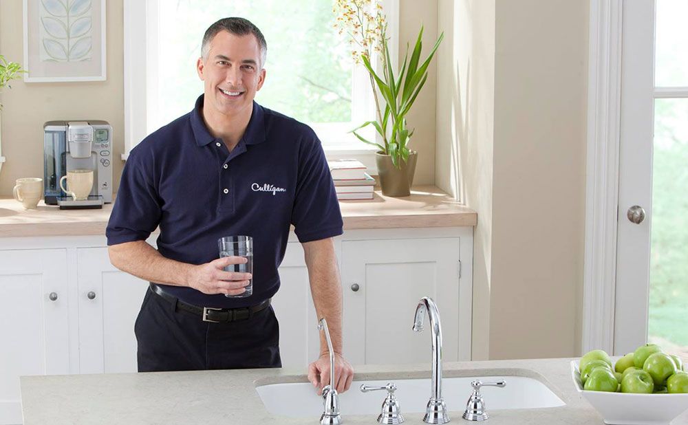 Culligan man holding cup of water near sink