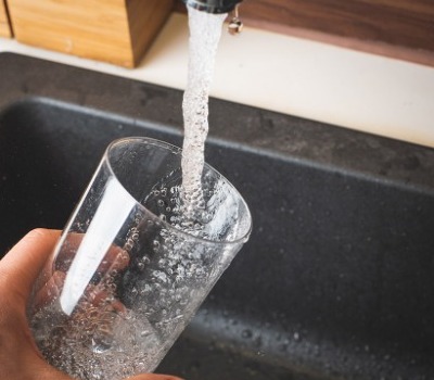 person filling drinking glass with water from tap