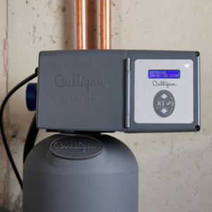 A gray Culligan high-efficiency water softener with a blue digital display showing 'SOFTENING' and a Wi-Fi symbol. Copper pipes are visible in the background.